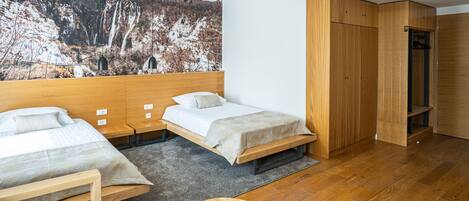 A modern hotel room with two beds, a wooden wardrobe, and a large wall mural of a mountainous landscape.