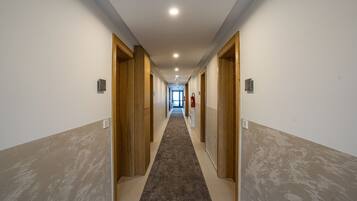 Un pasillo largo y estrecho con puertas de madera a ambos lados, que conduce a una habitación luminosa al final.