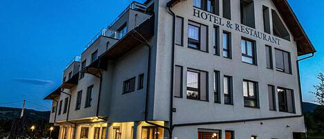 Un hotel de varios pisos con un restaurante en la planta baja, que presenta un diseño arquitectónico moderno con grandes ventanales y techo plano.