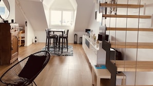 A modern loft apartment with a sloped ceiling, a dining area with a table and chairs, a black chair, a wooden staircase, and a view of the city through large windows. - ❤️ New! Luxury apartment with sea view in the heart of downtown (Concarneau)