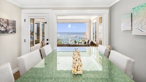 A dining area with a view of the sea and boats, a green marble table, and white chairs.