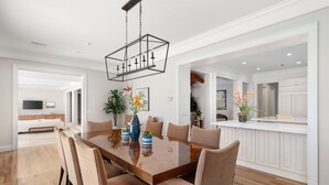 Un comedor espacioso con una gran mesa de madera, sillas tapizadas en beige y una lámpara de techo moderna.
