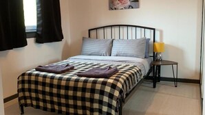 A bedroom with a checkered bedspread, a black metal headboard, a small bedside table with a yellow lamp, and a fluffy rug. - The Rabbit Hole - Kinlochbervie (Kinlochbervie)