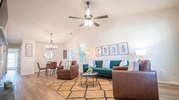 Ein geräumiges Wohnzimmer mit Deckenventilator, einem Essbereich mit Stühlen und Tisch, einem grünen Sofa und einem Teppich.