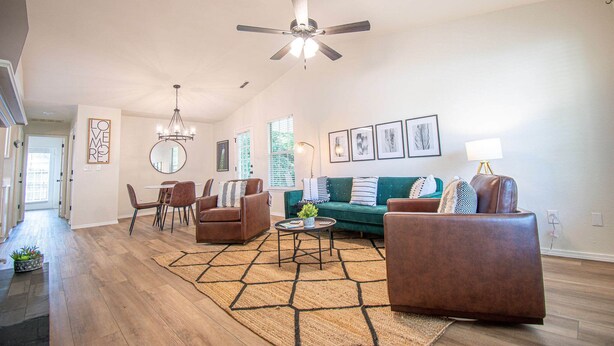 A spacious living room with a ceiling fan, a dining area with chairs and a table, a green sofa, and a rug.