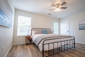 Um quarto com cama, ventilador de teto, janela e porta.