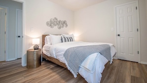 A bedroom with a bed, bedside lamp, ceiling fan, and a wall decoration.