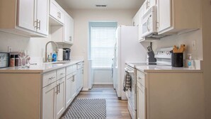 A narrow kitchen with white cabinets, a microwave, and a sink.