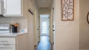 A narrow hallway with a kitchen area on the left, a door at the end, and a wall-mounted sign.