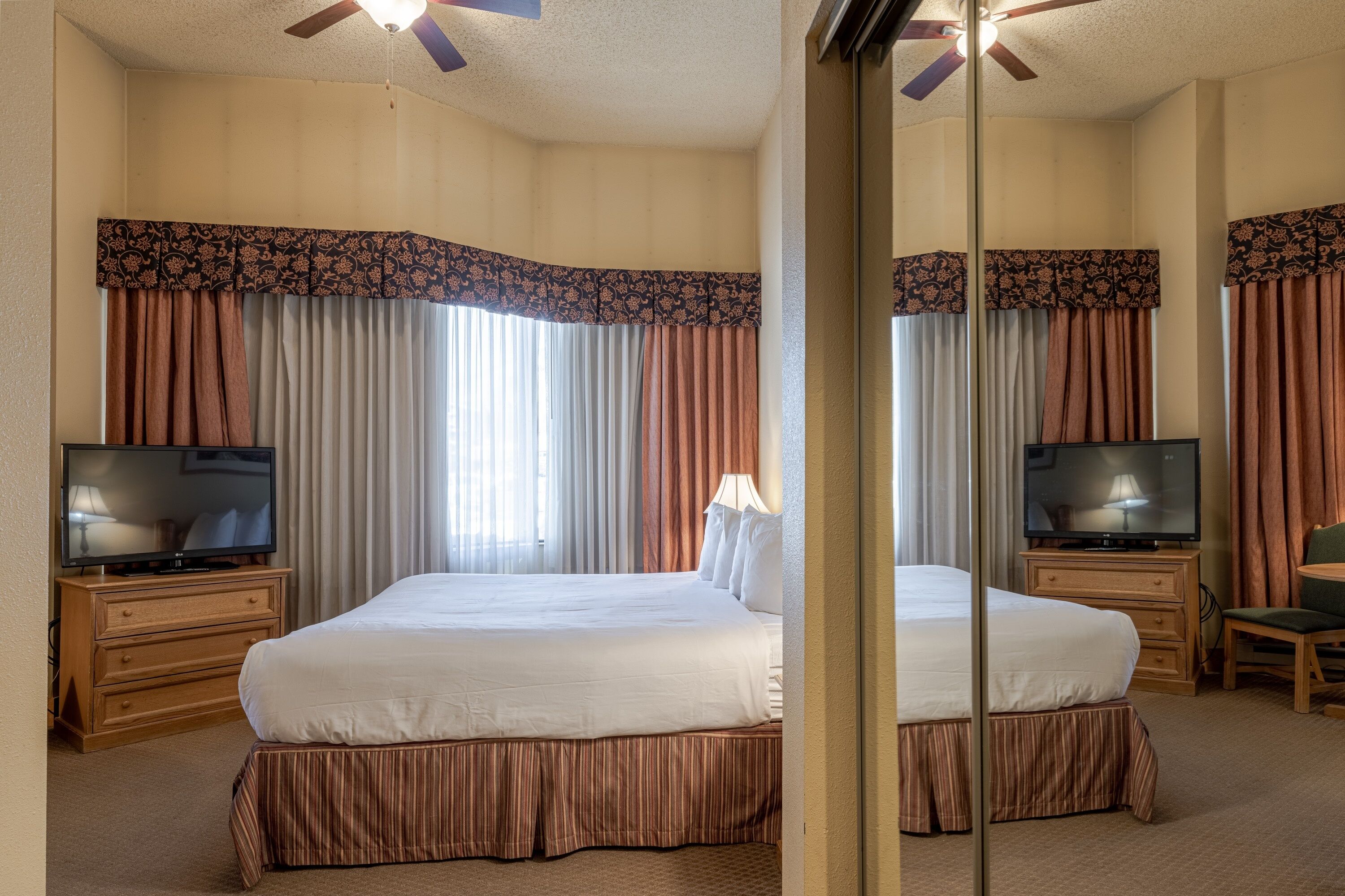 A hotel room with a large bed, two bedside tables with lamps, a television, and a ceiling fan.