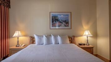 A neatly made bed with white linens, two bedside lamps, a telephone, and a framed landscape painting on the wall.