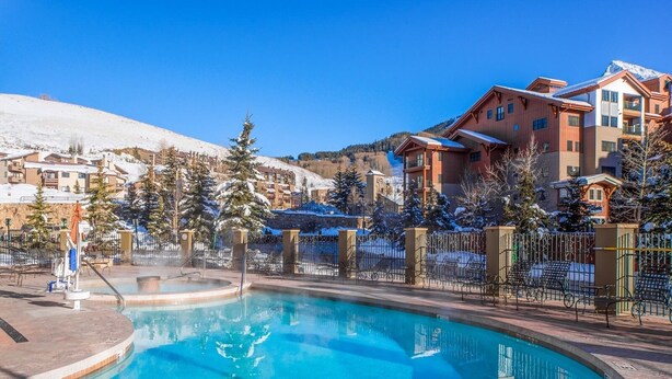 A pool area with a hot tub, surrounded by snow-covered trees and buildings. - Cozy Pet-friendly King Studio In Mt. Crested Butte Condo - No Cleaning Fee! by RedAwning (Crested Butte)