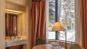 A hotel room with a round wooden table, two chairs, a window with a view of trees, a sink with toiletries, and a lamp. - Cozy Pet-friendly King Studio In Mt. Crested Butte Condo - No Cleaning Fee! by RedAwning (Crested Butte)