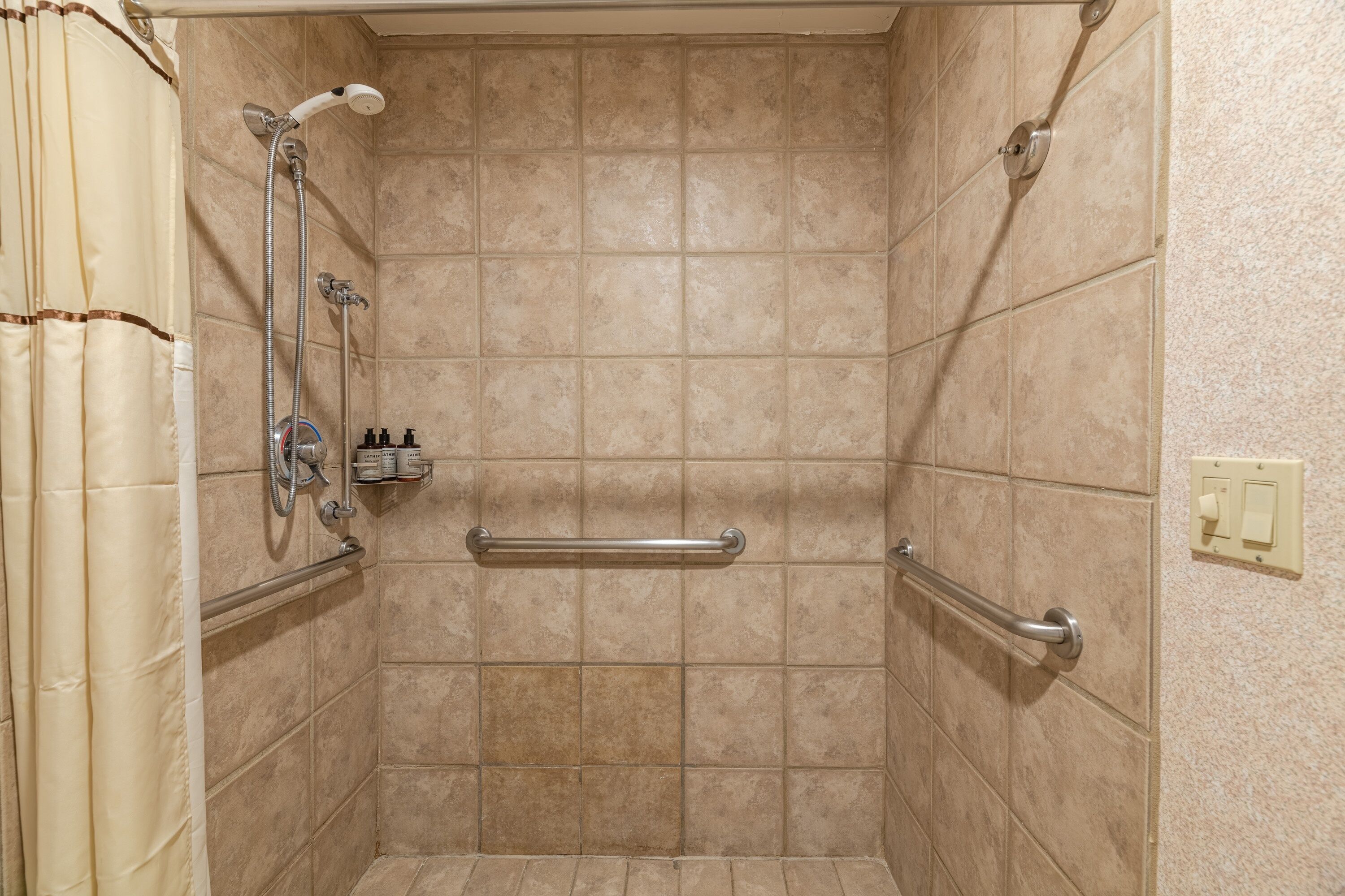 A shower with beige tiles, a grab bar, and a showerhead.