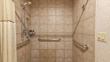 A shower with beige tiles, a grab bar, and a showerhead.