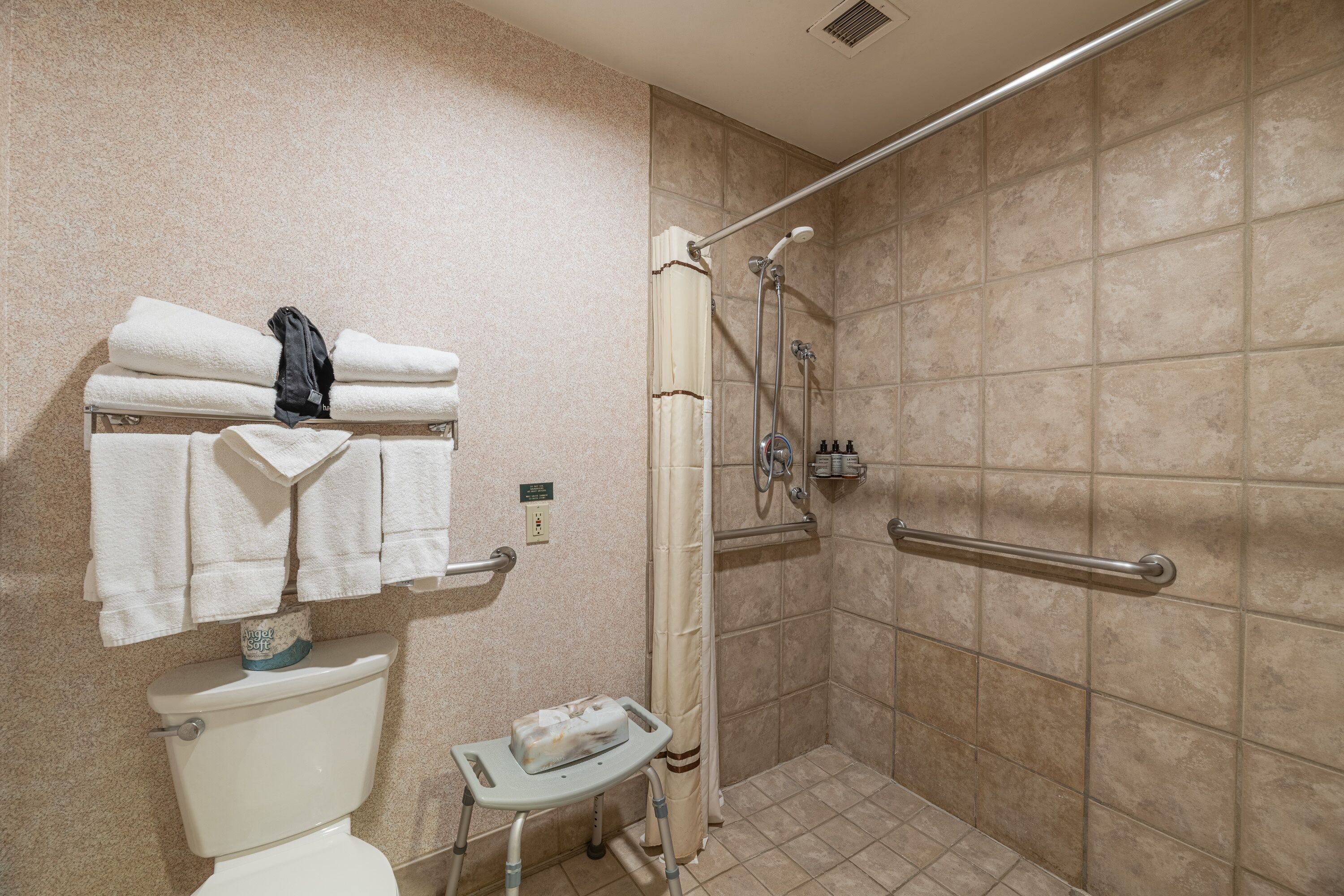 Een badkamer met een douche, toilet en een handdoekrek met opgevouwen handdoeken.