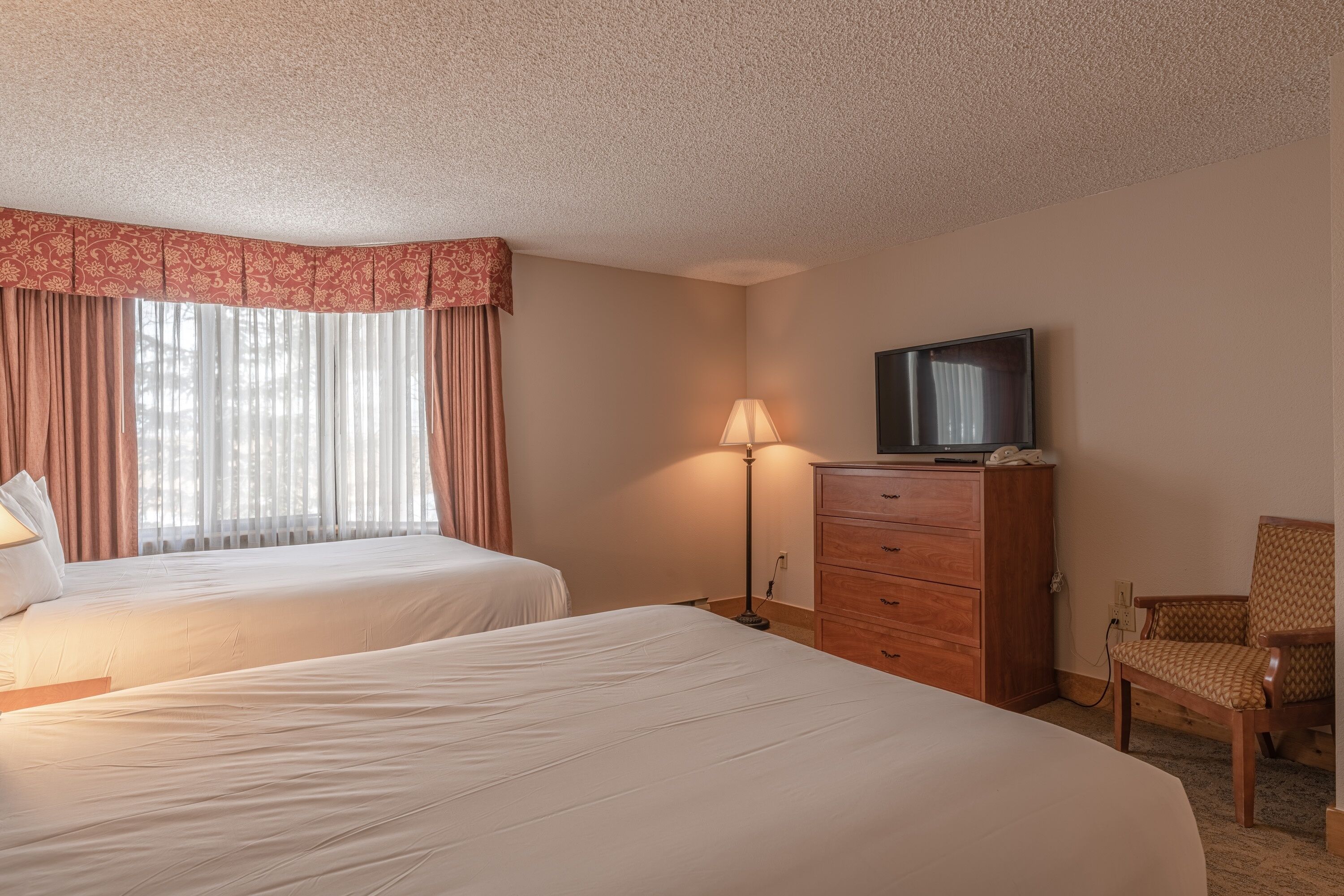 Habitación de hotel con dos camas, un televisor, una lámpara, un tocador y una silla.