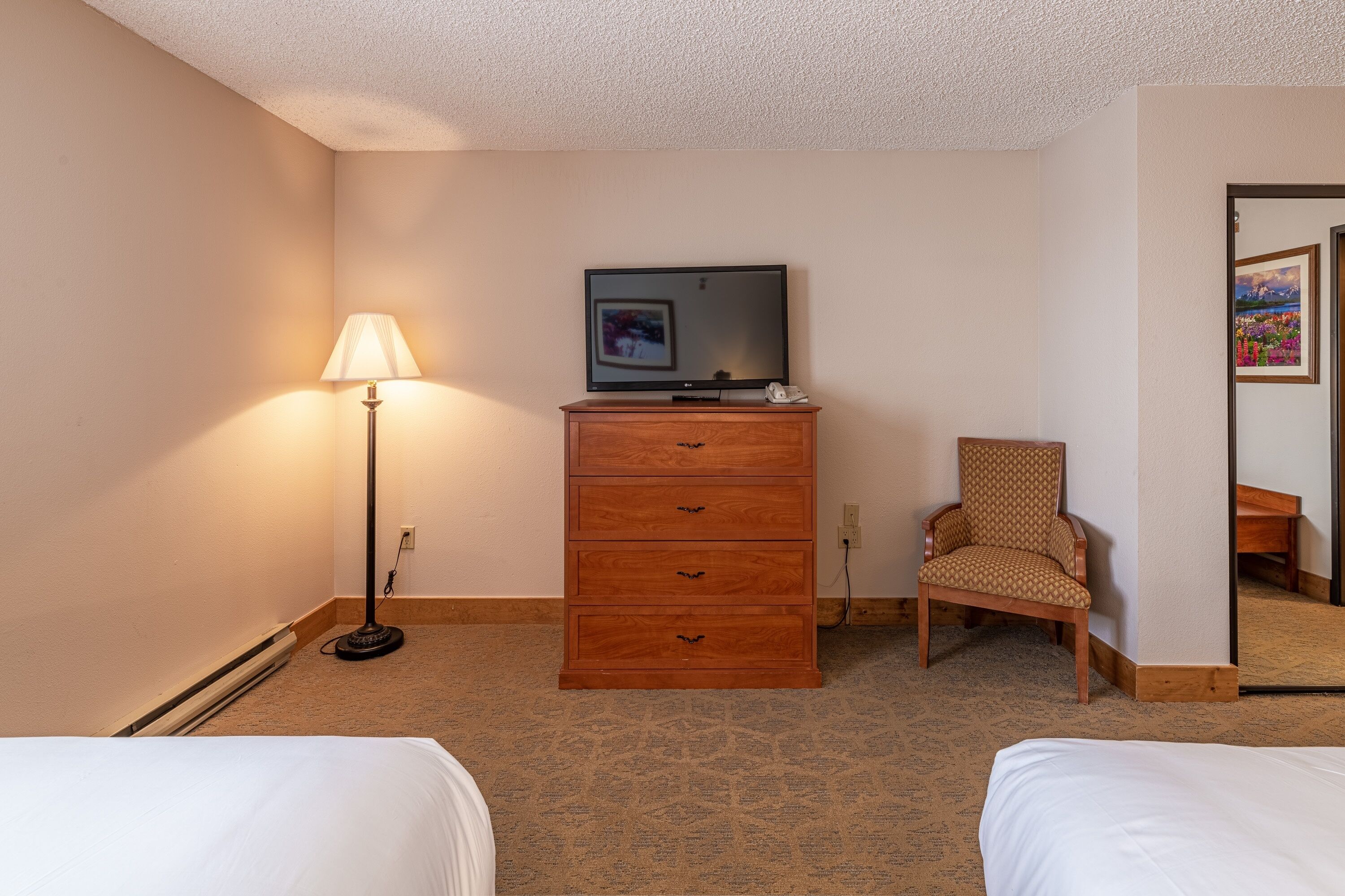 Habitación de hotel con dos camas, un aparador de madera, televisor, lámpara y una silla estampada.
