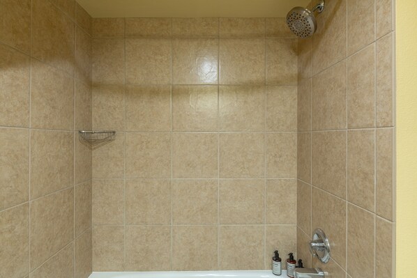 A bathroom with beige tiles, a showerhead, a sink with a mirror, and toiletries on the counter.