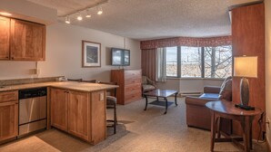 A compact kitchen with wooden cabinets, a built-in dishwasher, and a dining area with a table and chairs. - Grand Lodge 1-Bedroom Condo with 3 Queens & Close to Everything 1 Condo - No Cleaning Fee! by RedAwning (Crested Butte)