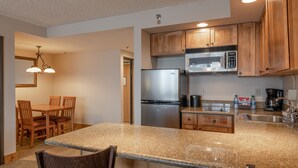 A kitchen with granite countertops, stainless steel appliances, wooden cabinets, and a dining area with a table and chairs. - Grand Lodge 1-Bedroom Condo with 3 Queens & Close to Everything 1 Condo - No Cleaning Fee! by RedAwning (Crested Butte)