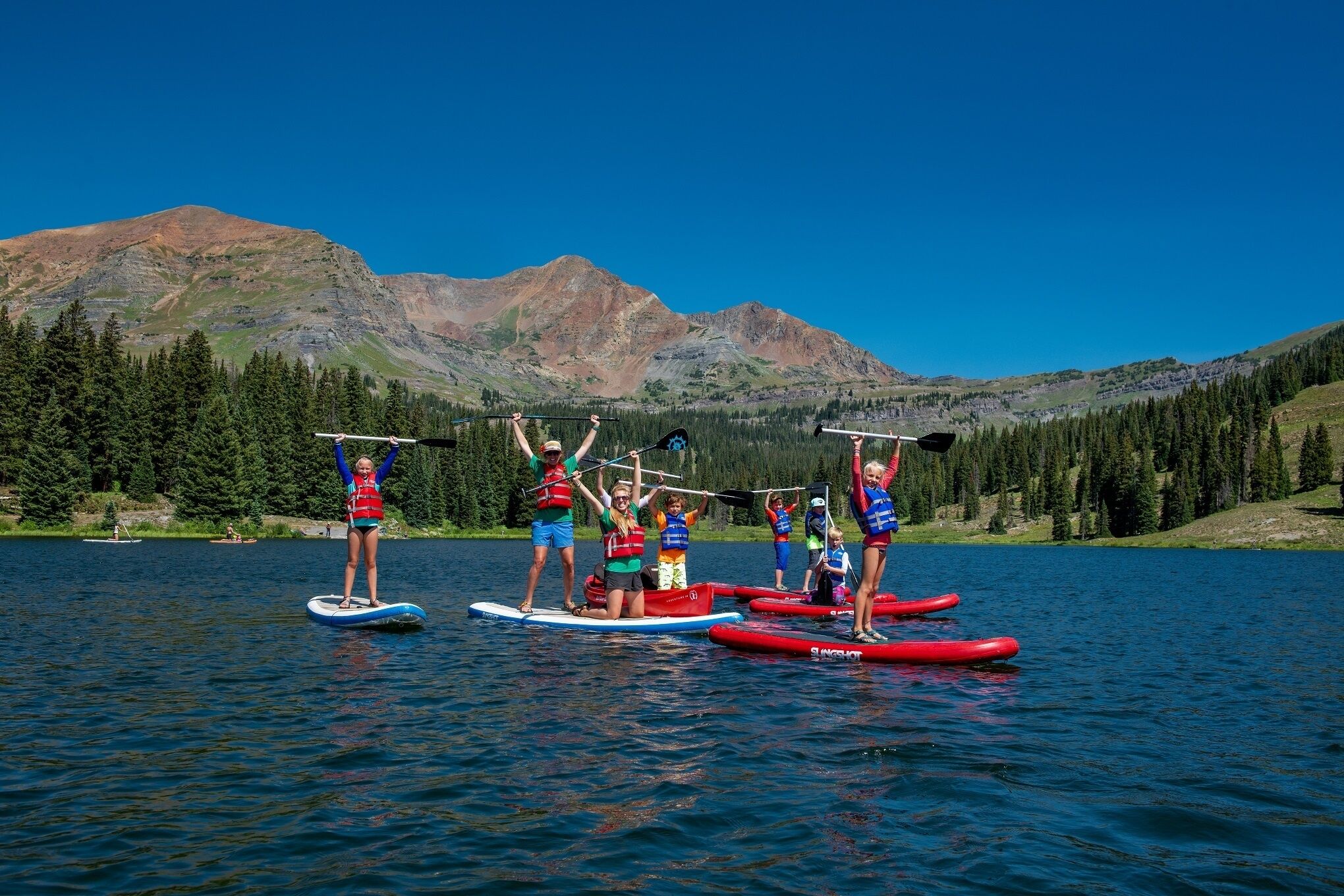 Un groupe de personnes pratique le paddle sur un lac, avec des montagnes en arrière-plan.