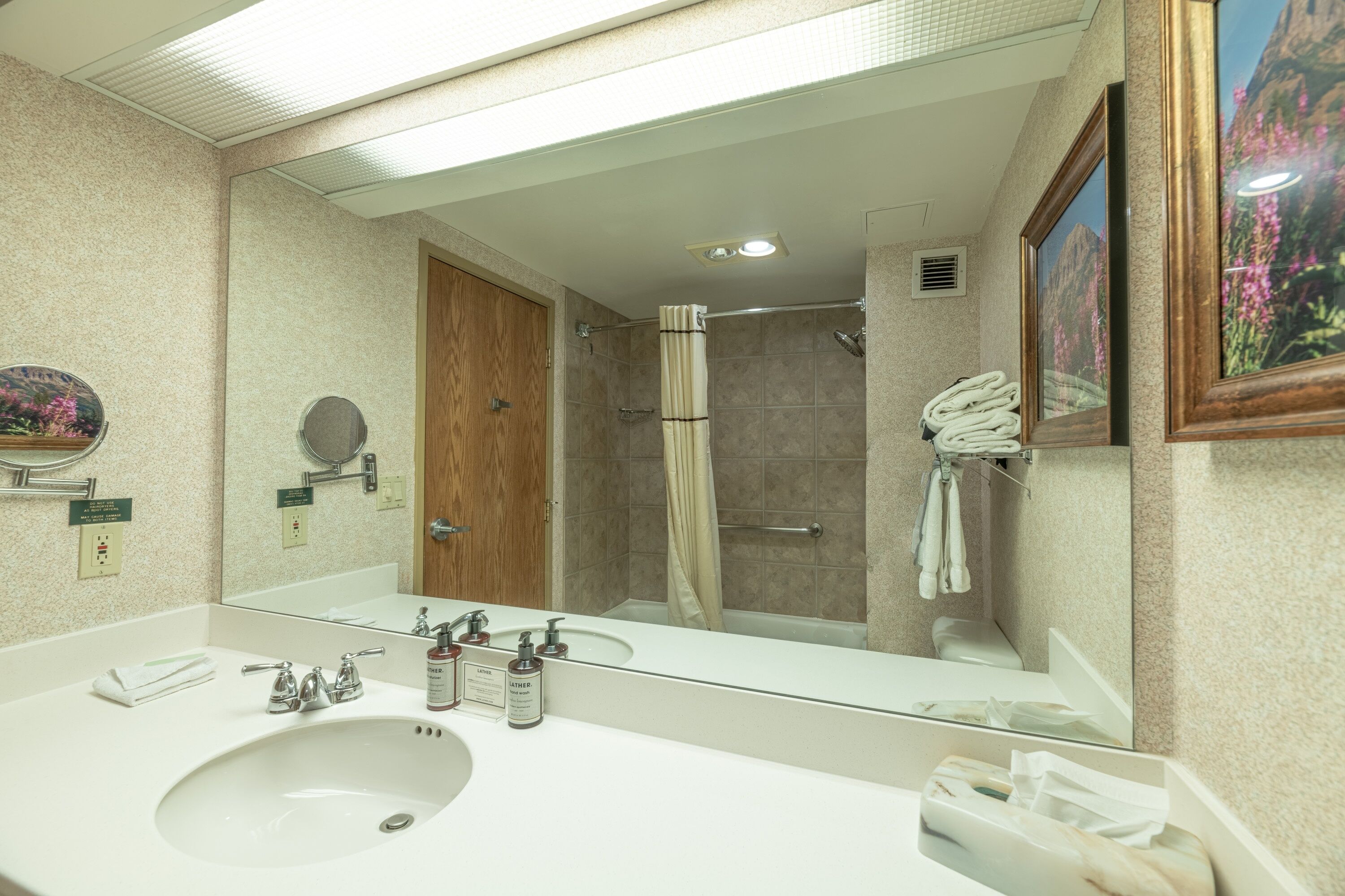 Un bagno con uno specchio grande, un lavandino, una doccia e un quadro appeso al muro.
