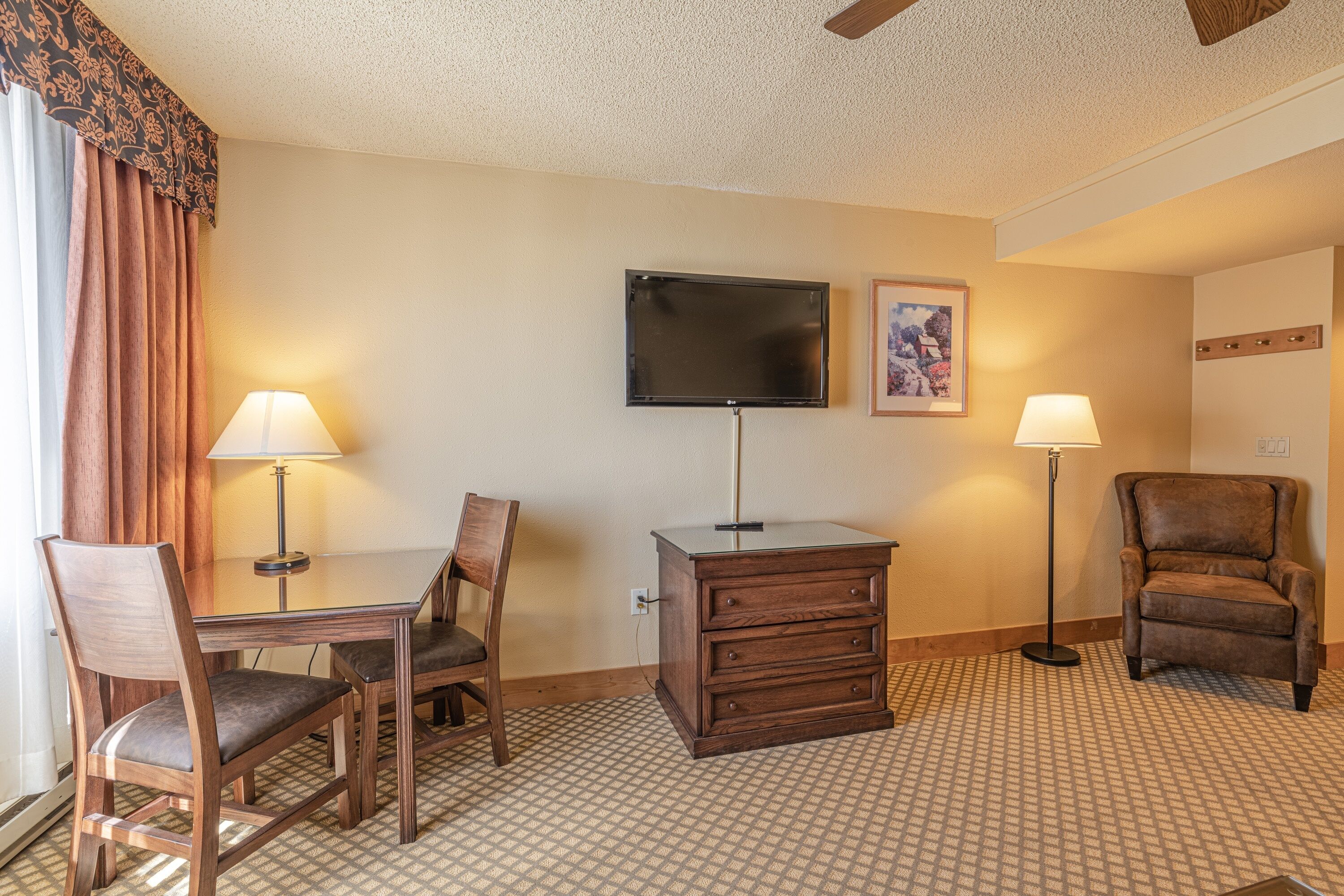 A hotel room with a desk, two chairs, a TV, a dresser, and two lamps.