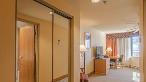 A hotel room with a wooden door, a desk with a chair, a television, and a window with curtains. - Grand Lodge Condo In The Heart Of Mt Crested Butte 1 Bedroom Condo - No Cleaning Fee! by RedAwning (Crested Butte)