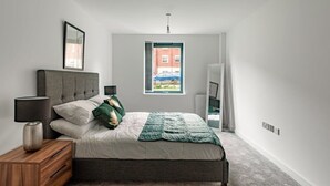 Un dormitorio con cama, mesita de noche, lámpara y ventana con vistas a edificios.