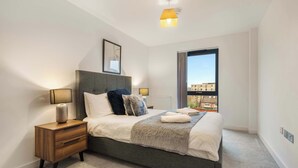 A modern bedroom with a large bed, bedside lamps, a nightstand, and a view of the city through a large window. - Stay Zeni, Ouse Court York Stylish 2 Bed Apartment (York)