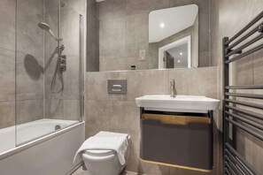 Un baño moderno con ducha envuelta en vidrio, inodoro blanco y lavamanos con cajón de madera.