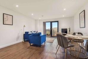 Una sala de estar moderna con un sofá azul, una mesa de comedor con sillas y un ventanal con vista a la ciudad.