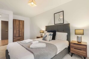 Un dormitorio moderno con una cama grande, mesitas de noche, un armario y una obra de arte enmarcada en la pared.