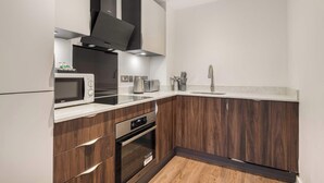 A modern kitchen with a microwave, toaster, sink, and wooden cabinets. - Stay Zeni, Ouse Court York Stylish 2 Bed Apartment (York)