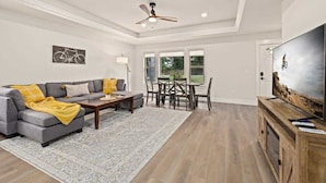 A spacious living room with a gray sectional sofa, a wooden coffee table, and a large flat-screen TV on a wooden stand. - OZ Adventure Retreat-Explore *Ride*Relax*Repeat (Bella Vista)