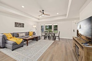 A spacious living room with a gray sectional sofa, a wooden coffee table, and a large flat-screen TV on a wooden stand.