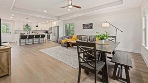 A spacious kitchen with modern appliances, a dining area with a wooden table and chairs, and a living area with a sofa and a plant. - OZ Adventure Retreat-Explore *Ride*Relax*Repeat (Bella Vista)