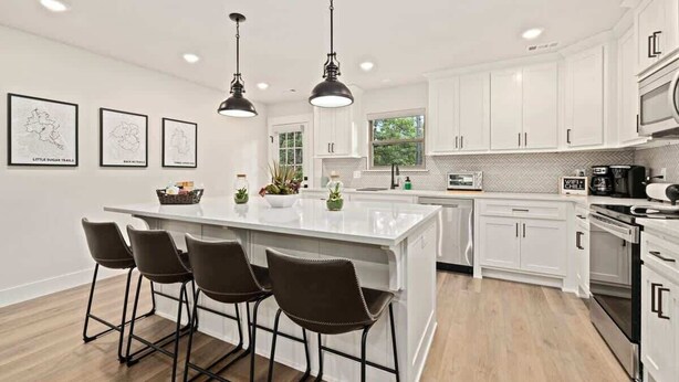A modern kitchen with white cabinets, a central island with bar stools, pendant lighting, and a microwave. - OZ Adventure Retreat-Explore *Ride*Relax*Repeat (Bella Vista)
