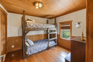A bunk bed room with wooden walls and a ceiling, a desk with a lamp, and a window with a view of greenery. - Escape to Calcasieu Lake Lodge-Premier Fishing and Family Getaway (Lake Charles)