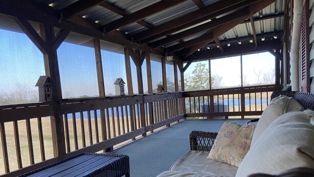 A covered outdoor seating area with a bench and a sofa, overlooking a beach. - Escape to Calcasieu Lake Lodge-Premier Fishing and Family Getaway (Lake Charles)