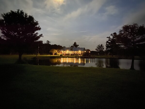 A lakeside building with a reflection in the water, surrounded by trees. - Escape to Calcasieu Lake Lodge-Premier Fishing and Family Getaway (Lake Charles)