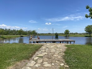 A wooden dock extending into a calm lake, surrounded by grassy banks and trees. - Escape to Calcasieu Lake Lodge-Premier Fishing and Family Getaway (Lake Charles)