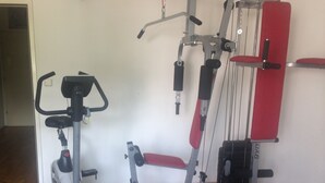 A home gym with a stationary bike, a bench press, a cable machine, and dumbbells.