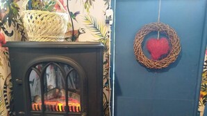 A room with a vintage stove, a blue door with a heart decoration, and floral wallpaper. - Pilgrims Shepherd's Hut - Goosewell Glynn Glamping (Callington)