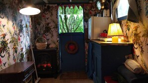 A compact kitchen with a stove, a hanging light fixture, and a window with a view of greenery. - Pilgrims Shepherd's Hut - Goosewell Glynn Glamping (Callington)