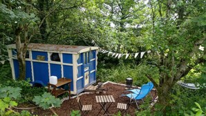 A rustic outdoor seating area with a blue playhouse, wooden tables, and blue chairs. - Pilgrims Shepherd's Hut - Goosewell Glynn Glamping (Callington)