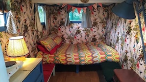 A compact room with a bed, a desk, and a chair. The walls are decorated with tropical wallpaper. - Pilgrims Shepherd's Hut - Goosewell Glynn Glamping (Callington)