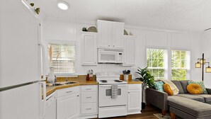 Cocina compacta con armarios blancos, microondas y estufa. En la sala de estar, hay un sofá gris con almohadones amarillos.