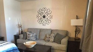 Una sala de estar con un sofá, una mesa de centro, una obra de arte en la pared y una lámpara.